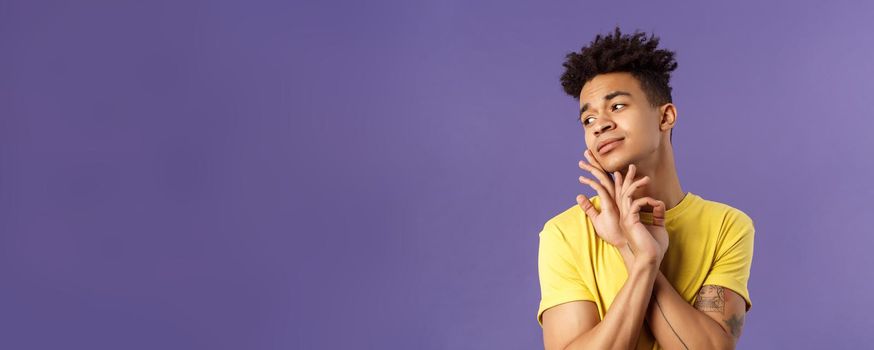 Close-up portrait of glamour beautiful young queer guy with dreads, standing in feminine model pose, gently touching face and looking away sensual, standing purple background.