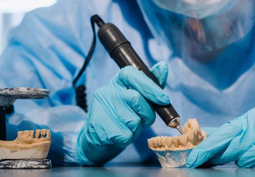 A masked and gloved dental technician works on a prosthetic tooth in his lab.