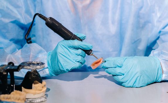 A masked and gloved dental technician works on a prosthetic tooth in his lab.