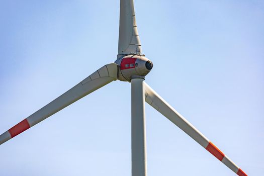 A close-up of a wind turbine with three huge rotor blades isolated against a blue sky