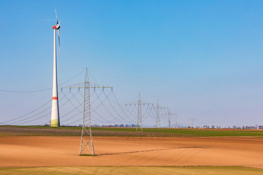 Several electricity pylons dominate the rural landscape with a huge wind turbine tower in the background