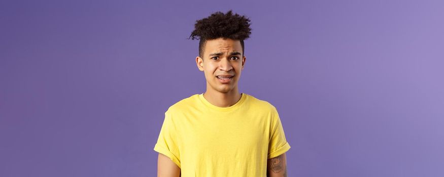 Close-up portrait of awkward and embarrassed young hispanic guy looking nervous, meeting girlfriend parents, stare scared and with panic, feeling concerned, cringe over purple background.