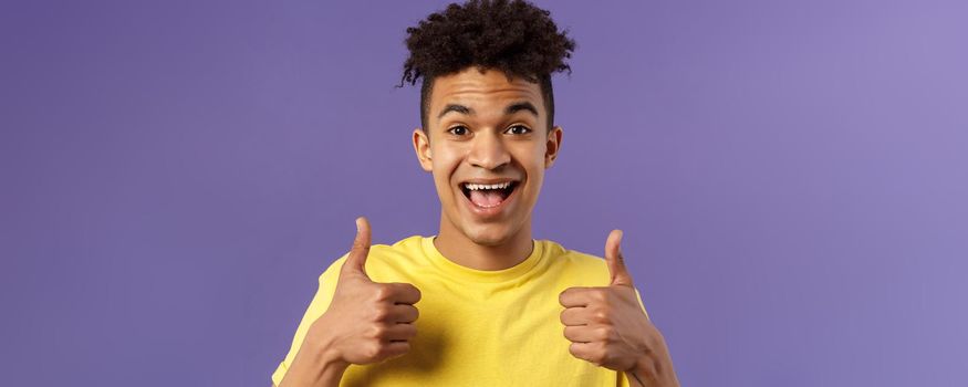 Close-up portrait of enthusiastic, lively hipster guy with afro haircut agree with something, show thumbs-up smiling with joy, recommend good product, like and approve plan, purple background.
