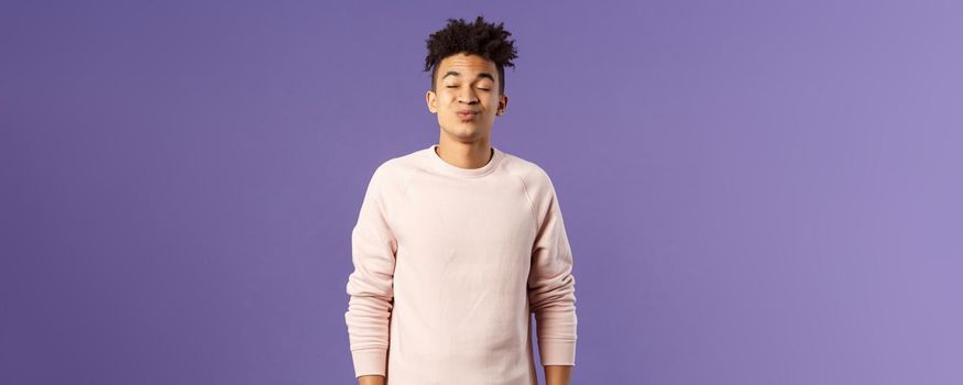 Portrait of cute and silly, young hispanic trying to kiss girl after date for the first time, leaning with folded lips and closed eyes towards her, making funny smile, standing purple background.