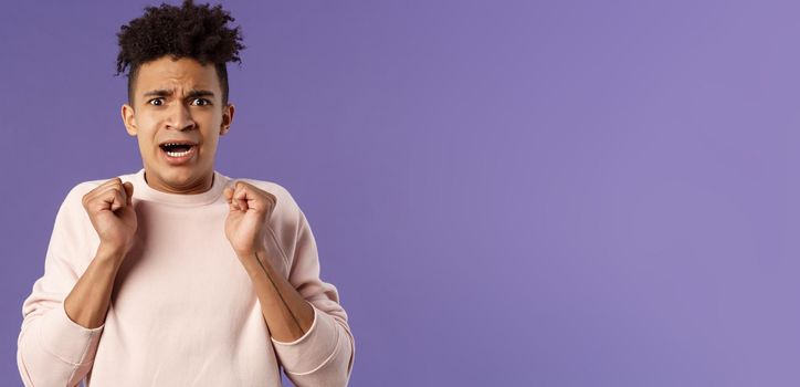 Close-up portrait of worried, anxious funny hispanic man jumping from fear, gasping look concerned, starting to panic before important meeting, standing purple background afraid and nervous.