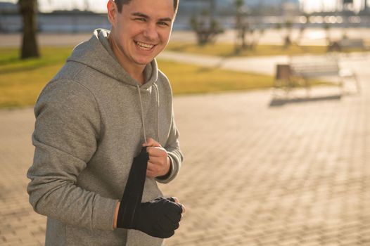 Caucasian man in hoodie bandaging his hands before boxing class outdoors