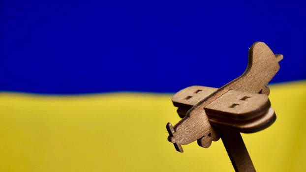 Decorative wooden toy plane on the yellow blue background of the Ukrainian flag. Russia attacked Ukraine in 2022