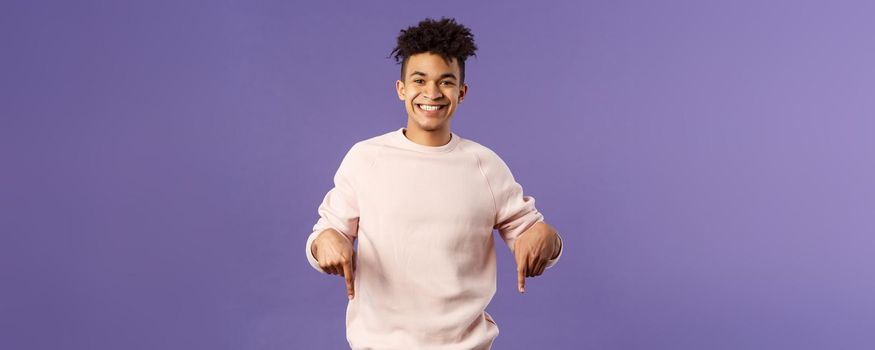 Portrait of cheerful, happy young 25s man recommending product, showing promo of product, delivery service, online shop or appllication, pointing fingers down, smiling pleased camera.