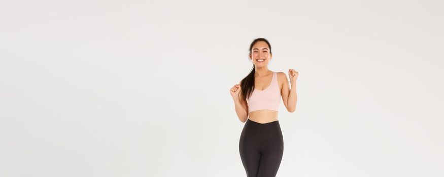 Sport, gym and healthy body concept. Full length of encouraged and motivated asian brunette girl ready for fitness training, fist pump and shouting in rejoice, gain goal with workout training app.
