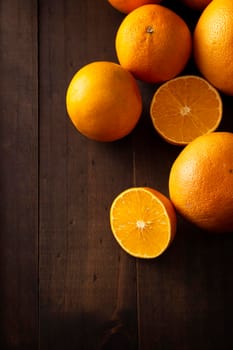 a ripe orange cut in half and several whole oranges on brown rustic wooden table with copy space