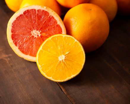 close up of ripe orange and grapefruit slices and several whole oranges on brown rustic wooden table with copy space