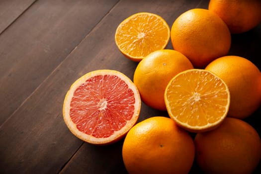 ripe orange and grapefruit slices and several whole oranges on brown rustic wooden table with copy space