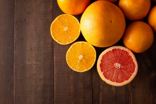 top view image of ripe orange and grapefruit slices and several whole oranges on brown rustic wooden table with copy space