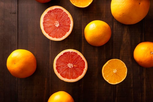 top view image of ripe orange and grapefruit slices and several whole oranges on brown rustic wooden table