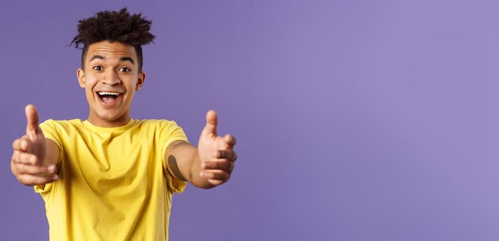 Close-up portrait of charismatic, happy friendly-looking hispanic man with dreads reaching hands forward to hold something, give hug or cuddle dearly, standing purple background.