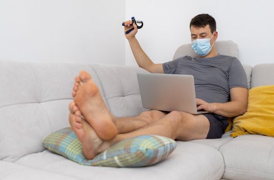 young man in mask and with laptop sitting on sofa. High quality photo