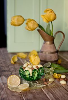 Easter still life, almonds in white chocolate and green easter eggs,yellow tulips in a wooden vase, background,High quality photo