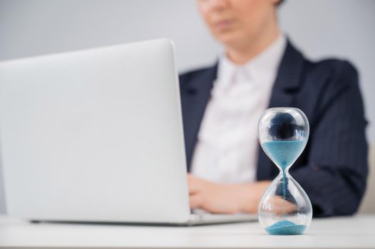 Business woman keeps track of time on an hourglass while working