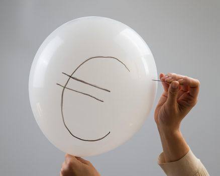 A woman bursts with a needle a balloon with the inscription euro
