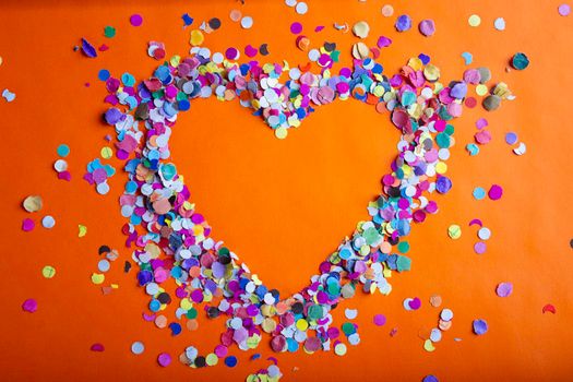 love concept image of heart shape frame made of colorful confetti on orange paper texture background