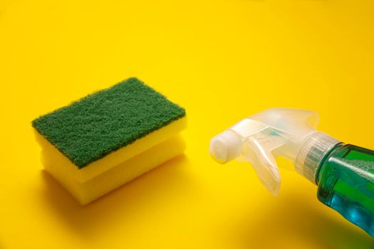 liquid detergent in sparay bottle and sponge on yellow background