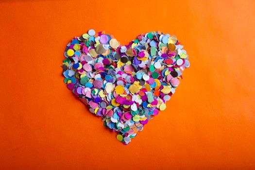 love concept image of heart shape made of colorful confetti on orange paper texture background