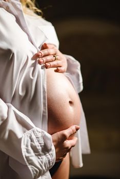 Pregnant woman in white shirt, holding belly with hands