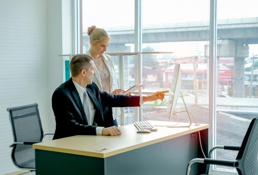 Business manager man point to the screen and discuss with his secretary in the office with glass window.