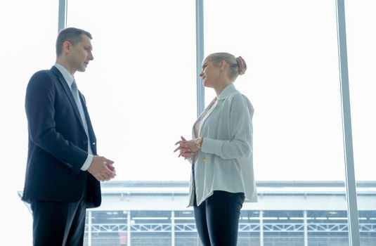Business man and woman talk together in front of grass windows with day light.
