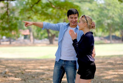 Handsome man point to the direction that make his girlfriend feel surprise and happy in the garden.
