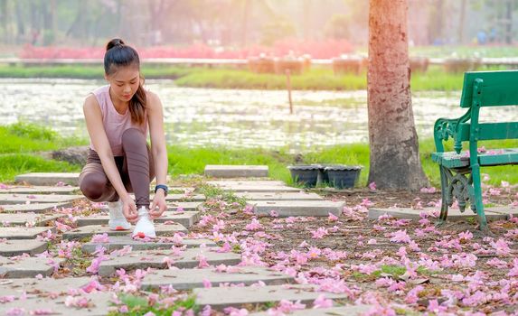 Portrait of beautiful sport girl is tying shoelace on bricks and pink flower spread to the floor in the garden with morning light.
