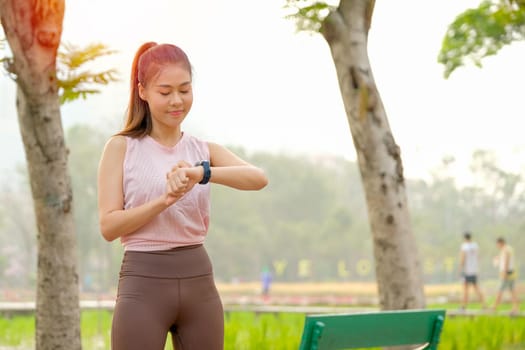Portrait of young beautiful sport girl look to her watch and stay in park or garden with morning light.