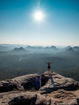 Shirtless male silhouette with raised arms on sharp mountain top. Sport life concept and outdoor activities