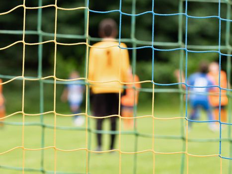 View through soccer gate net. The goalkeeper slowly backs up during the opponents' attack. Abstract view