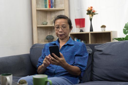 Elderly woman asian holding cell phone on sofa in home. Business communication and internet social networking technology.