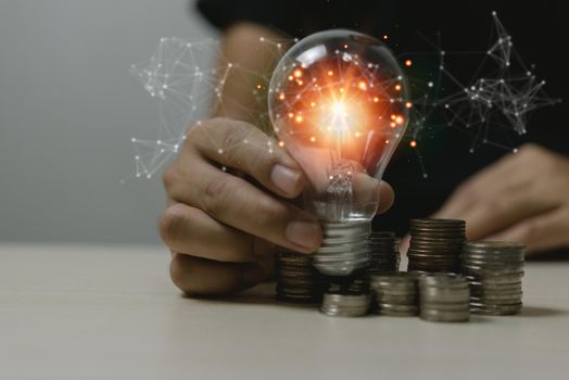 Innovation creativity growth idea success economy development strategy business concept.Hand holding light bulb on coin stack saving money on desk.