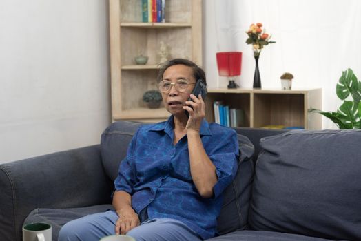 Elderly woman asian holding cell phone on sofa in home. Business communication and internet social networking technology.