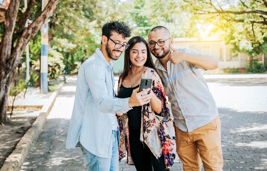 Happy friends watching a cell phone in the street. Three happy friends sharing the cell phone in the street. Concept of happy friends sharing media on a phone