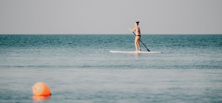 Silhouette of woman standing, surfing on SUP board, confident paddling through water surface. Idyllic sunset or sunrise. Sports active lifestyle at sea or river.