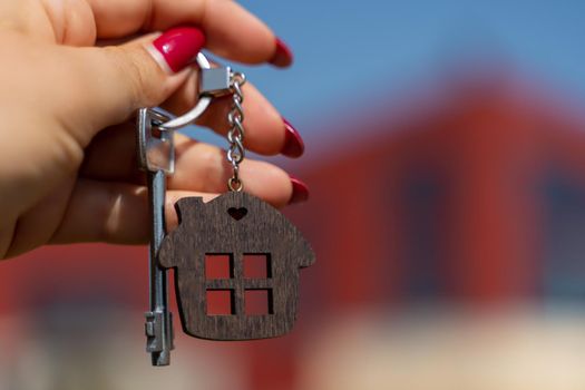 A woman's hand holds a house key against the backdrop of a house under construction. Real estate agent. Buying a house, apartment