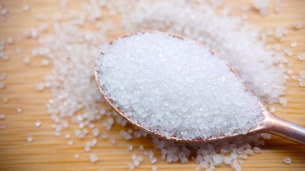 Macrophotography.A spoon with sugar granules on a wooden table. Close-up of sugar crystals.Background or texture