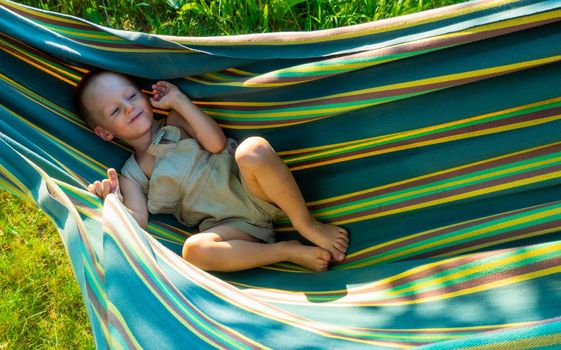 Cute little blond caucasian boy having fun with multicolored hammock in backyard or outdoor playground. Summer active leisure for kids. Child on hammock. Activities and fun for children outdoors. High quality photo
