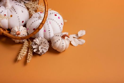White decorative hand made pumpkins with shiny stones and pine cones in basket on colored background. Autumn harvest concept.