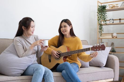 A young woman playing guitar on the sofa in the living room. Young Asian loving lovers couple bonding at home, relaxing on sofa the living room..