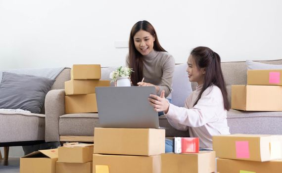 Startup small business owner working with computer at workplace. Freelance two woman seller check product order. Packing goods for delivery to customer. Online selling. E-commerce. Online Shopping.