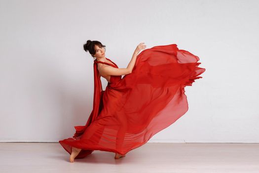 Dancer in a red flying dress. Woman ballerina dancing on a white studio background.