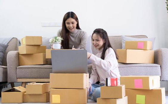 Startup small business owner working with computer at workplace. Freelance two woman seller check product order. Packing goods for delivery to customer. Online selling. E-commerce. Online Shopping.