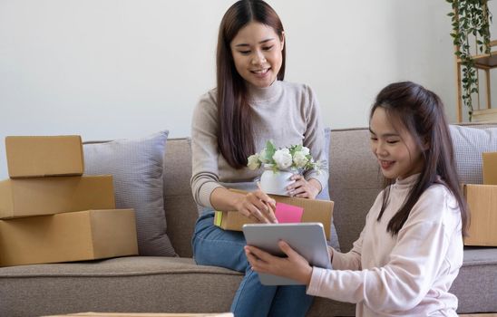 Startup small business owner working with computer at workplace. Freelance two woman seller check product order. Packing goods for delivery to customer. Online selling. E-commerce. Online Shopping.