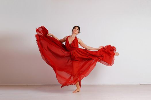 Dancer in a red flying dress. Woman ballerina dancing on a white studio background.