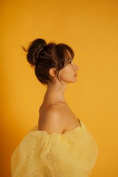 Profile portrait of a beautiful middle-aged woman in a yellow dress, her hair pulled up against a yellow background.